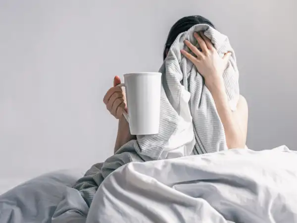 Woman holds cup coffee while lying bed